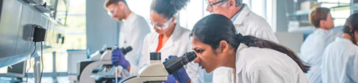 A female scientist looking into a microscope in a busy laboratory setting