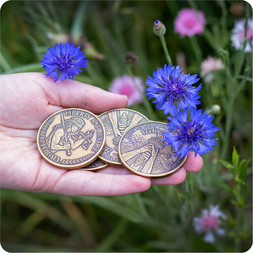 Hand holding a stack of brass USA coins next to blue cornflowers