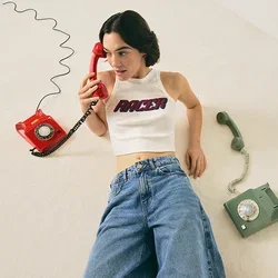 Frau in weißem Crop-Top und Jeans, die auf dem Boden liegt und ein rotes Wählscheibentelefon hält, mit einem grünen Wählscheibentelefon neben sich.