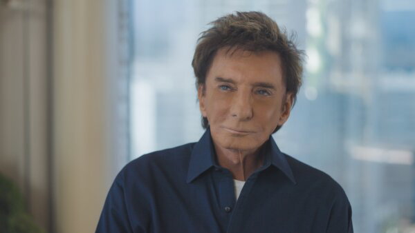Barry Manilow seen from the shoulders up in a dark blue button-up shirt.