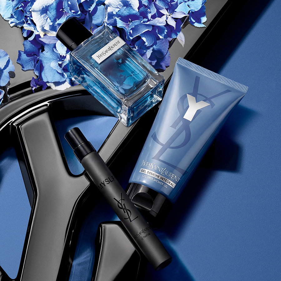 A YSL Y perfume, shower gel, and MYSLF travel spray arranged with blue hydrangeas.
