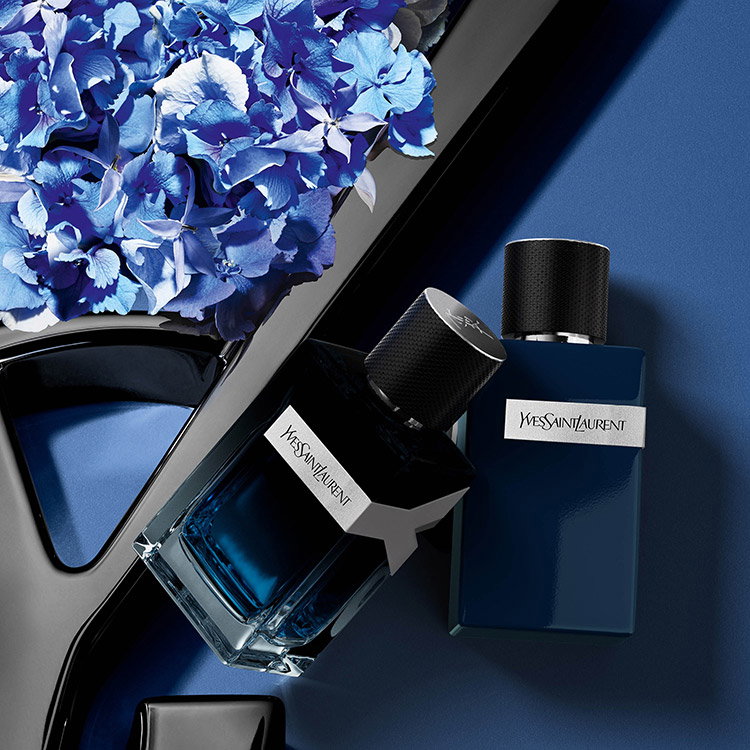 Two YSL Y fragrance bottles on a blue background with delicate blue flowers.