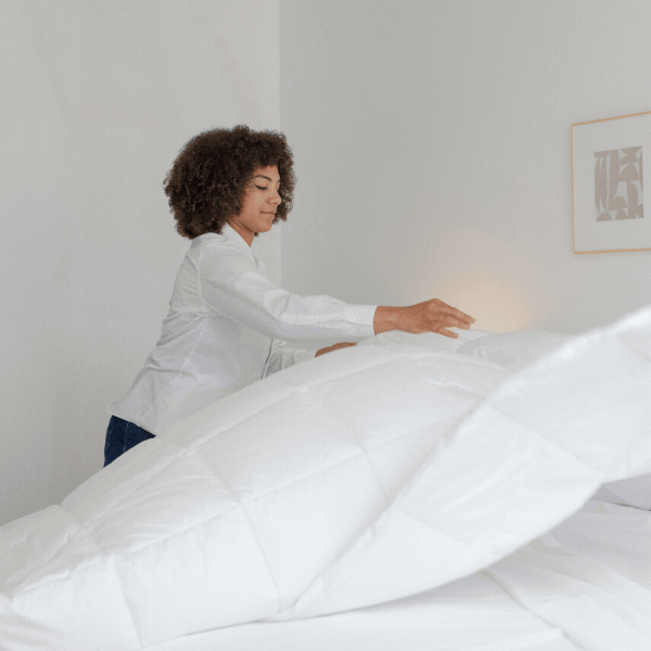 A woman makes her bed with a white duvet cover