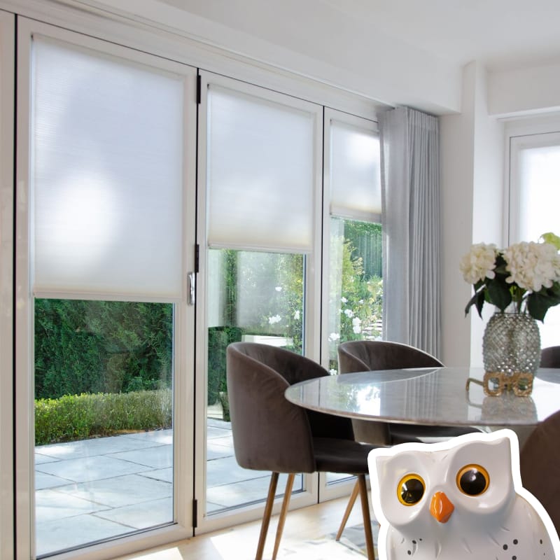 INTU Micro Hive blinds in kitchen diner bifold doors with grey voile curtain pushed over to one side. Table and chairs positioned in front with a vase in the centre.