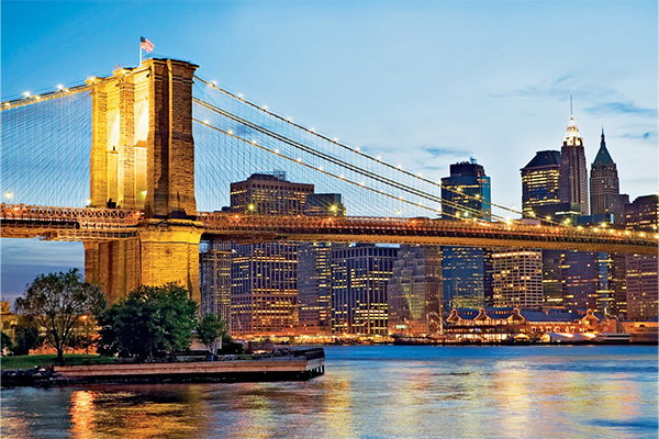 Beleuchtete Hängebrücke vor einer Skyline bei Abenddämmerung, mit Spiegelung im Wasser. | Link zu AIDA