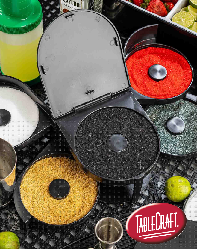 Tablecraft rimming station with multiple compartments filled with colorful salts and sugars, surrounded by bar tools, lime wedges, and cocktail ingredients.