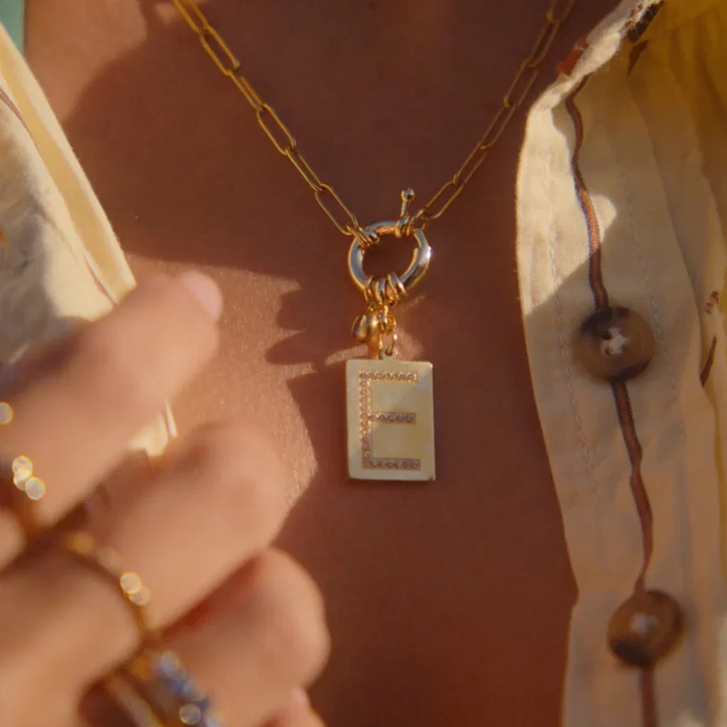 Gold chain necklace with rectangular pendant featuring geometric design on warm brown background