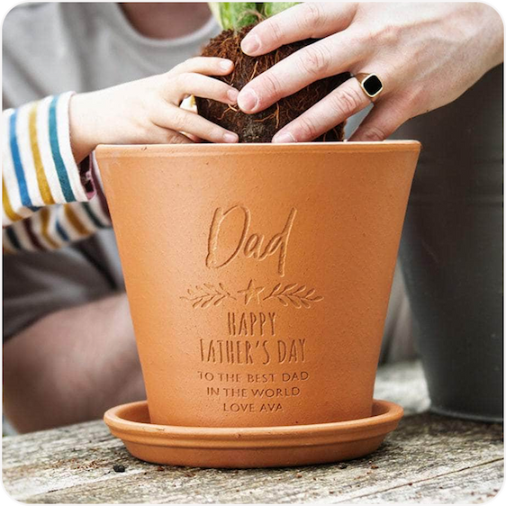 Hands planting a small plant into an engraved terracotta pot personalised for dad