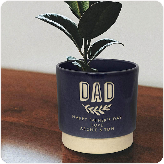 A dark ceramic pot engraved with "Dad" displayed with a small indoor plant