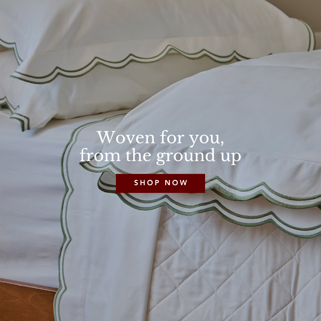 White bed linens with decorative green scalloped borders and a diamond-quilted blanket.