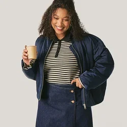 Lächelnde Frau in marineblauer Jacke, gestreiftem Oberteil und Rock hält eine Kaffeetasse, sie steht vor einem einfarbigen hellen Hintergrund.