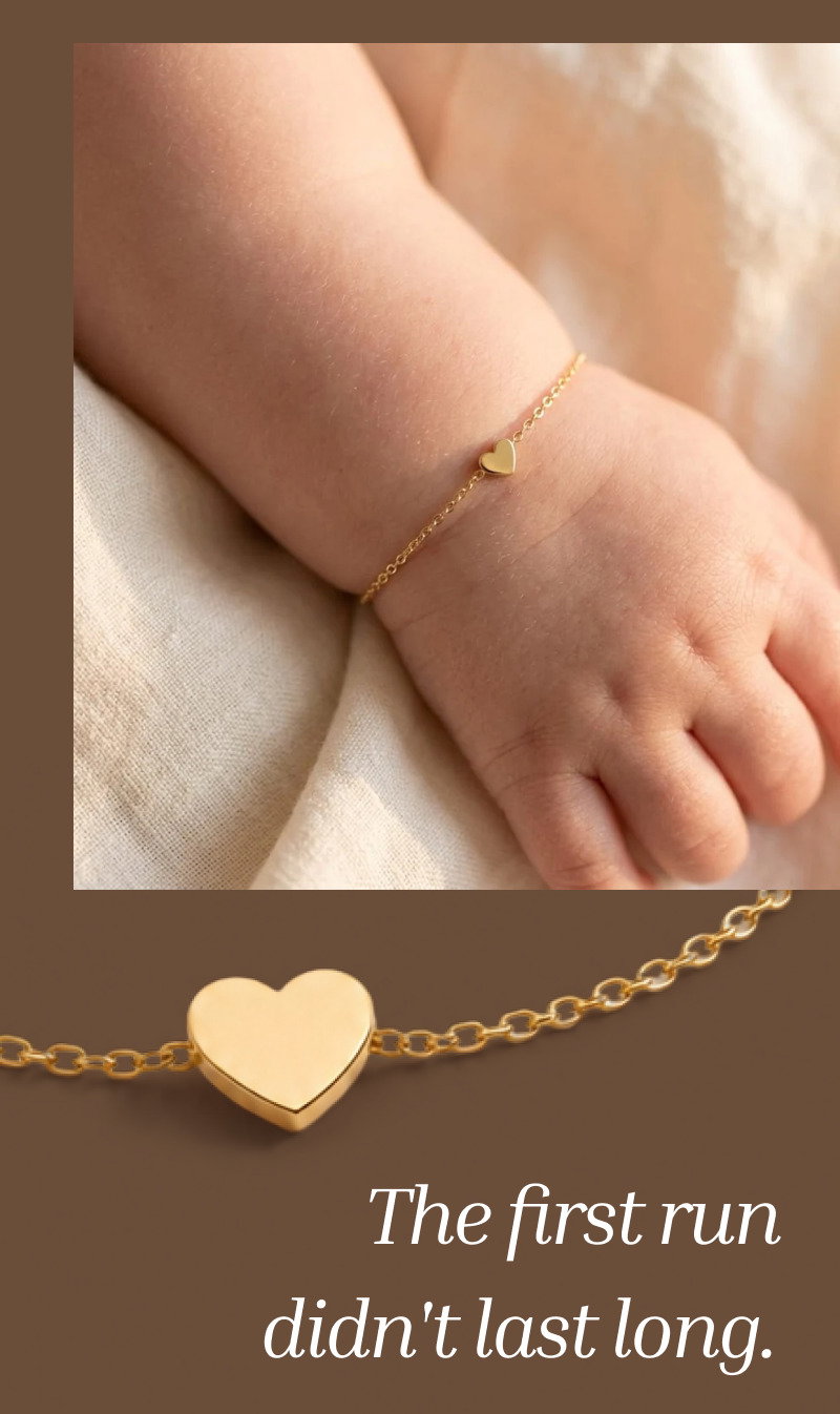 Close-up of a baby’s wrist wearing a delicate heart bracelet above large serif text about the first release selling out quickly.