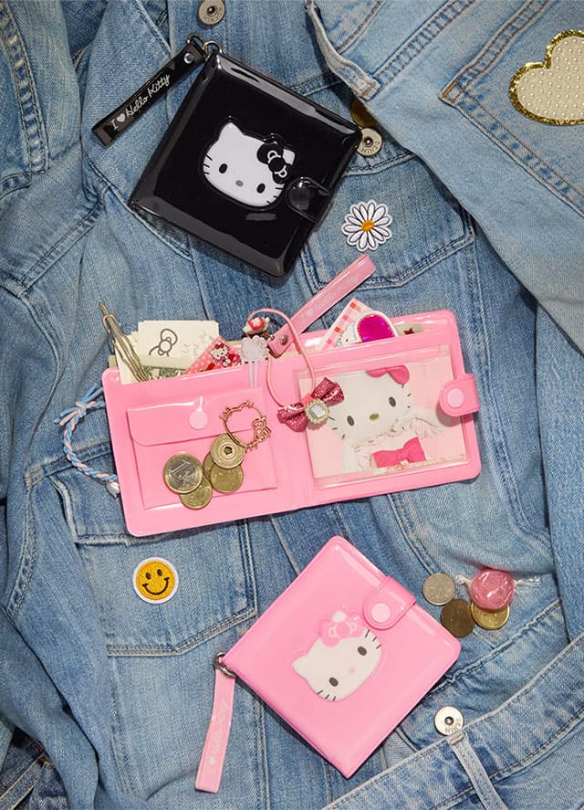 Three vinyl Hello Kitty wallets with the second one opened up, all laying on a background of denim jackets laid flat.