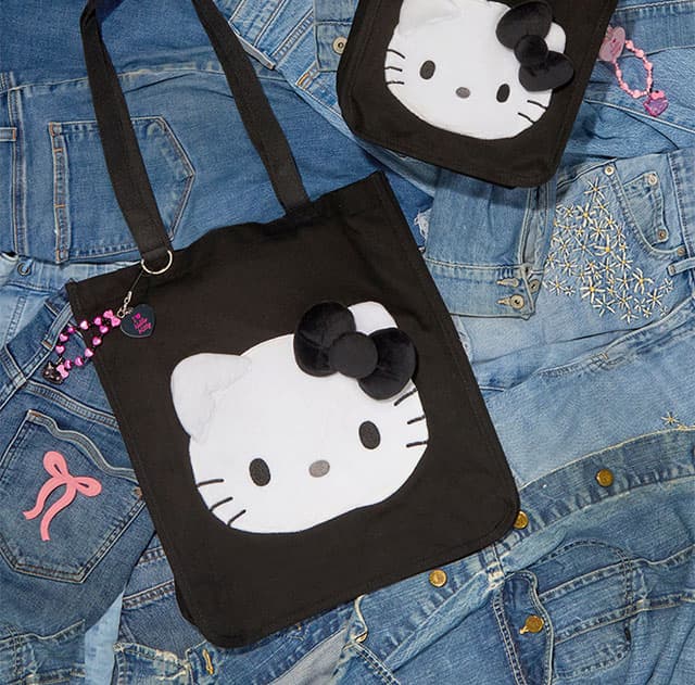 Black Hello Kitty tote bag on a background of denim jackets laid flat.