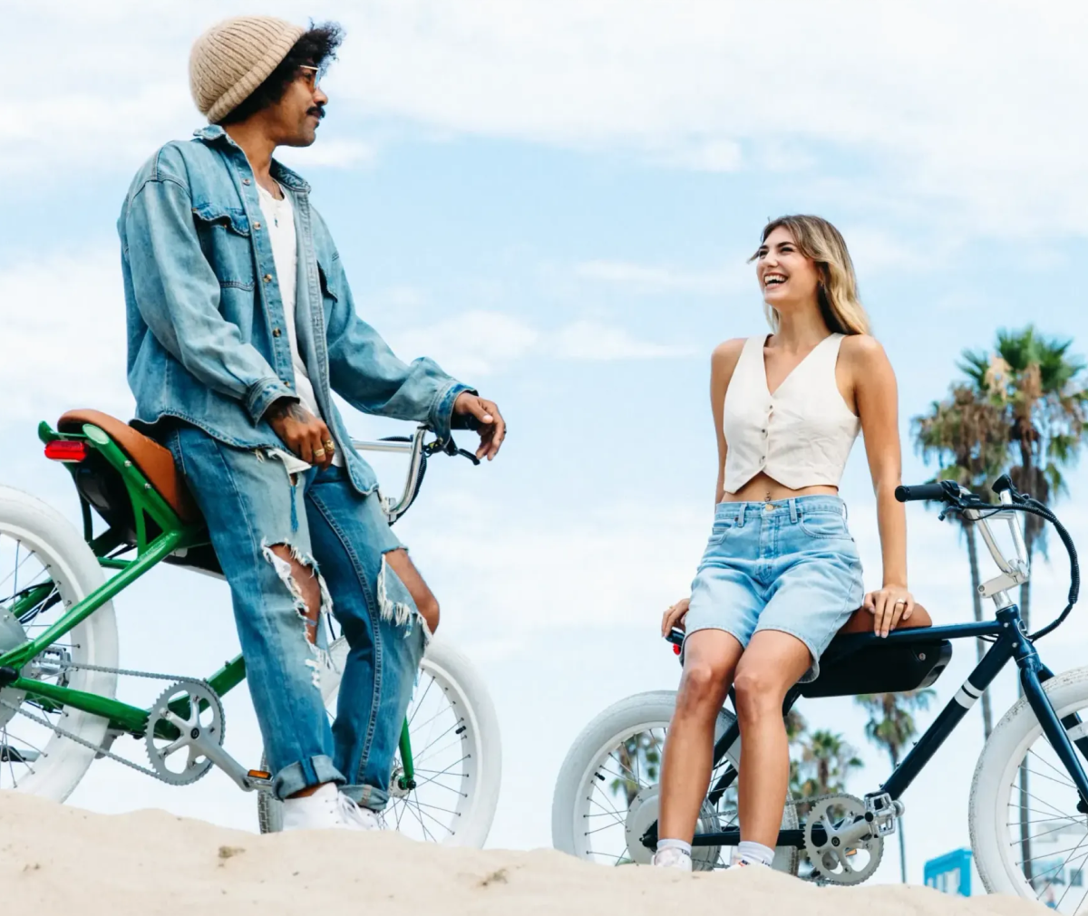 Two people on solé bicycles at the beach, smiling and enjoying the day.