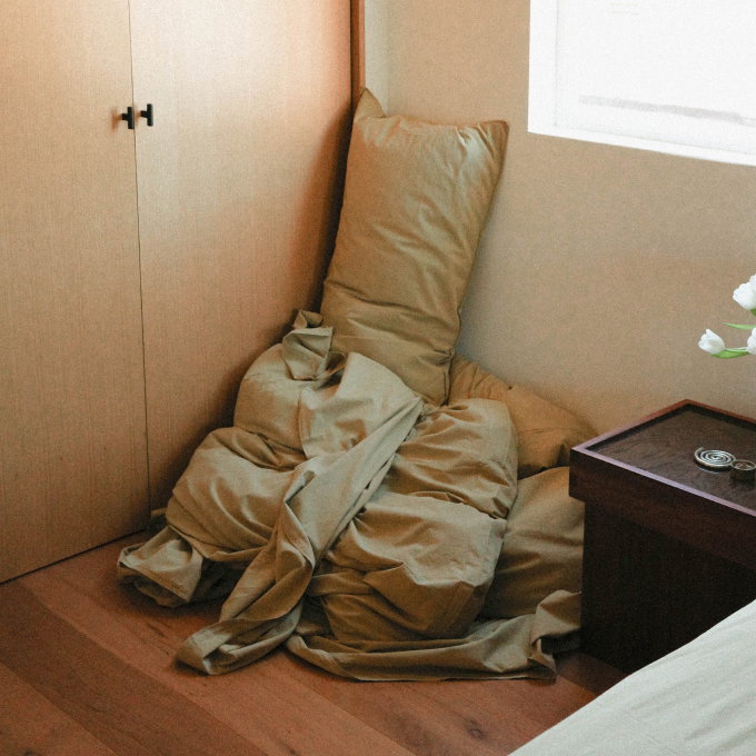 Light green sheets and pillow stacked in the corner of a bedroom