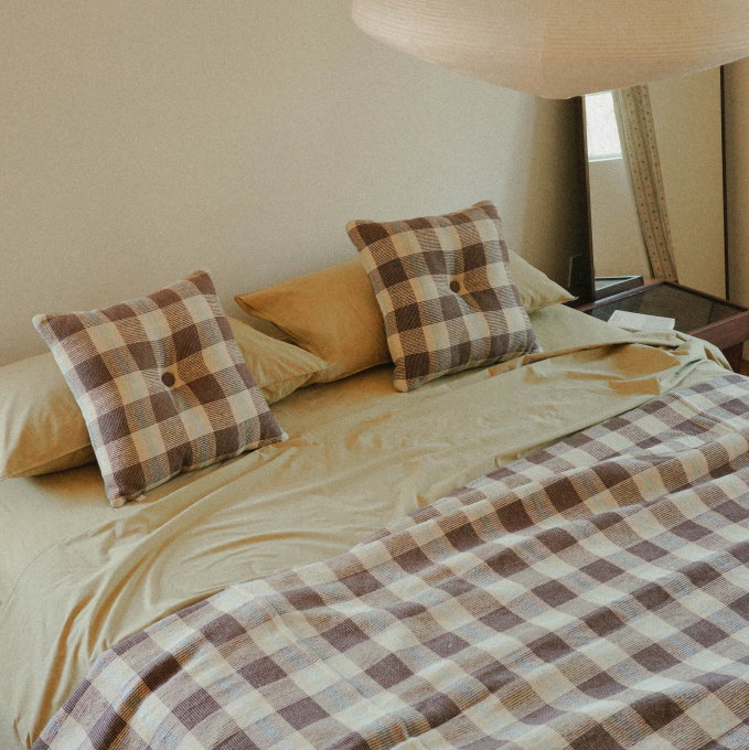 Detail of two square brown check throw pillows on light green sheets