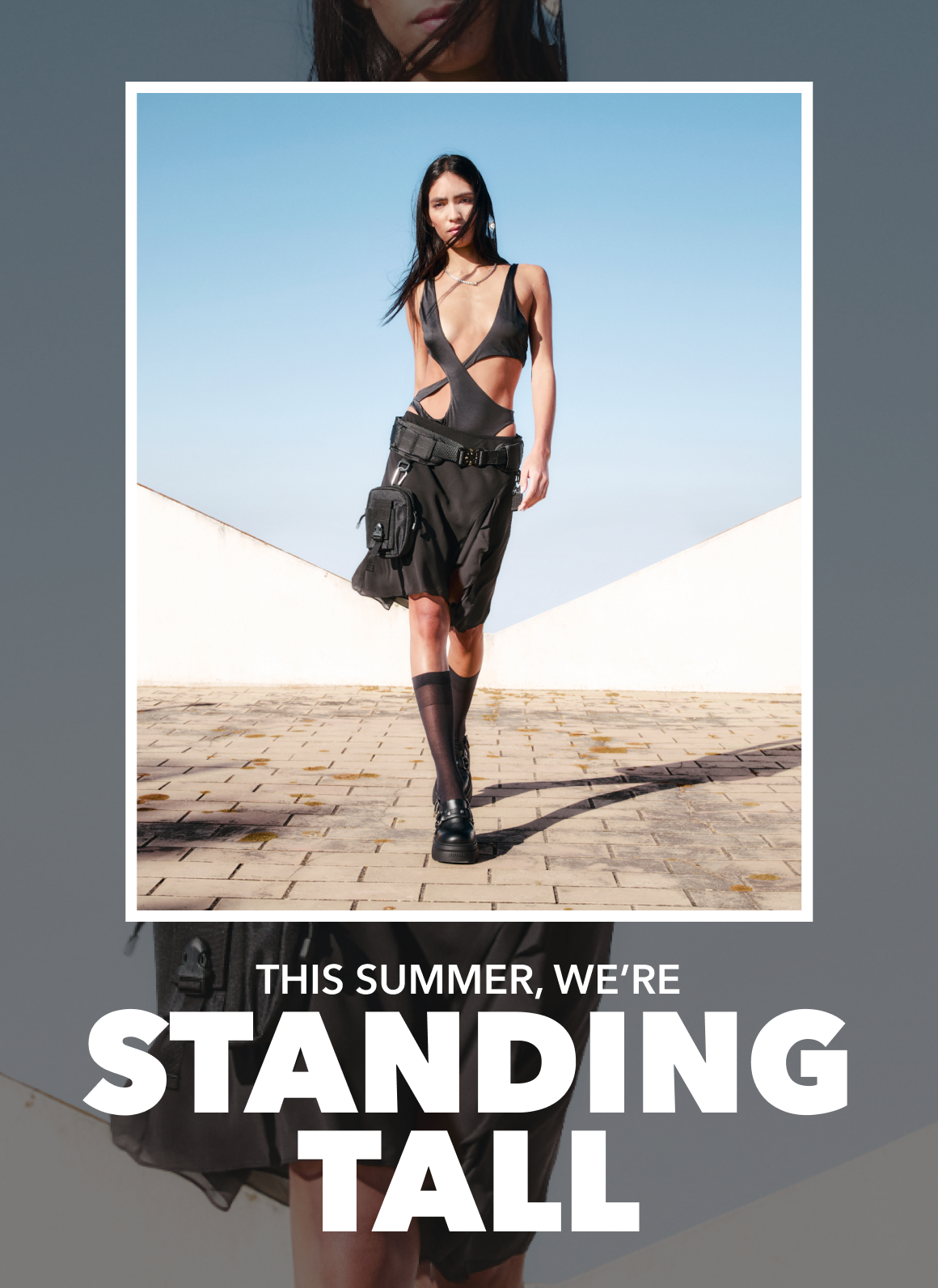 Black outfit summer look with utility skirt, knee-high socks and chunky shoes, walking outdoors against a minimalist backdrop