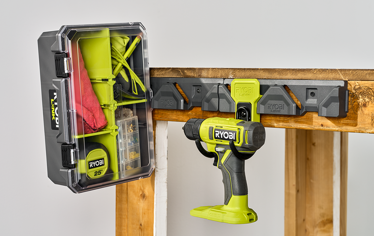 Woman in a navy shirt holding a RYOBI cordless vacuum while organizing tools and accessories on a RYOBI wall storage system in a garage