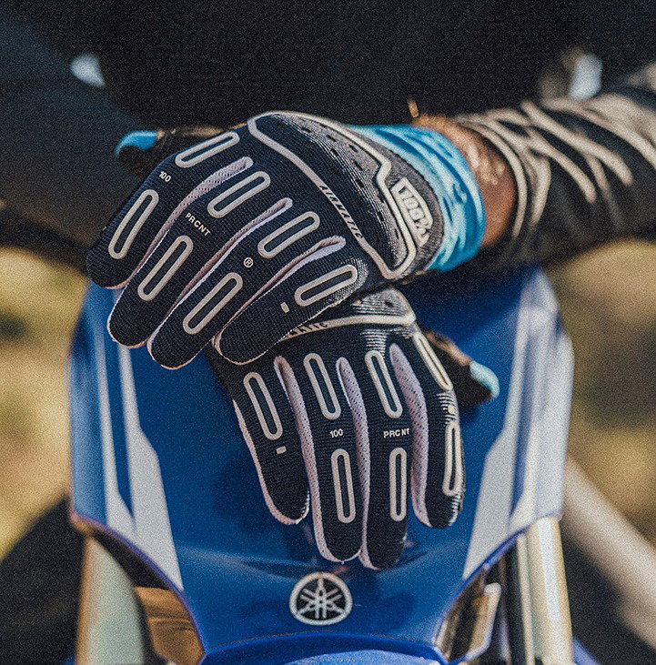 Off-road rider wearing 100% Airmatic 2 gloves on a trail through brush