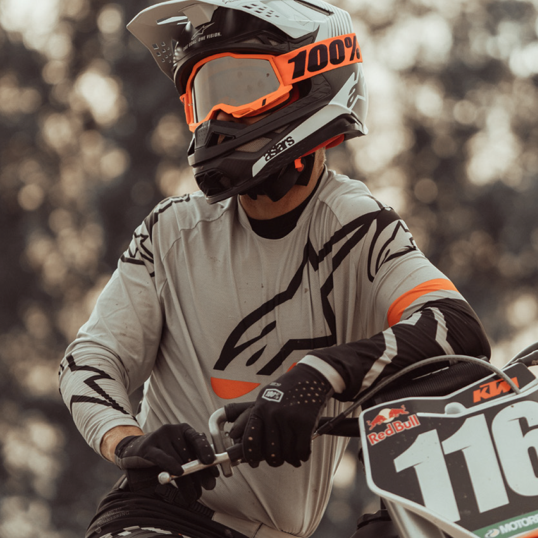 Motocross rider wearing 100% Sling gloves mid-race on a dirt track
