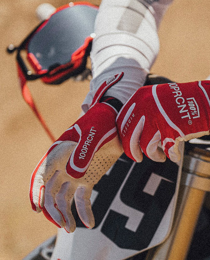Rider gripping motocross handlebars wearing 100% gloves on a dirt track