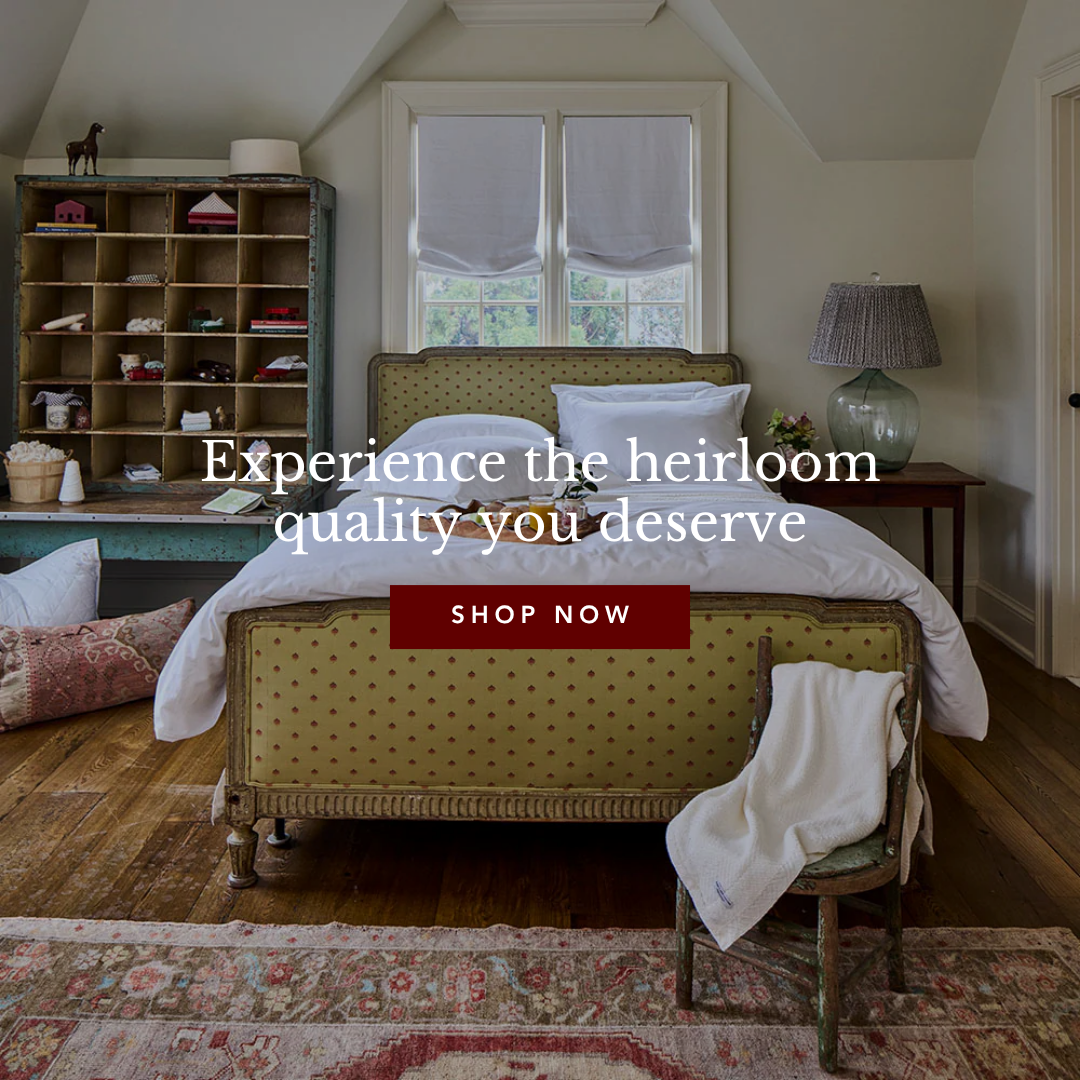 A vintage-style bedroom with a green patterned bed, antique hutch, and bedside lamp, featuring a colorful rug.