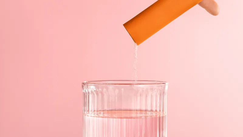 a hand pouring a collagen supplement powder into a glass