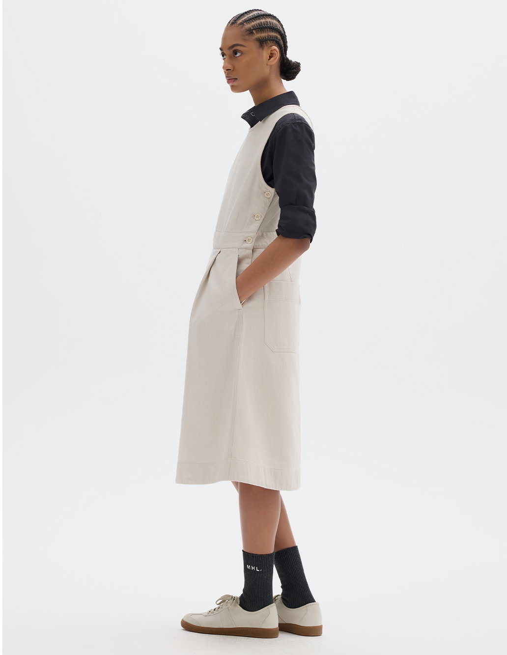 Off-white midi dress worn over a dark shirt and paired with trainers