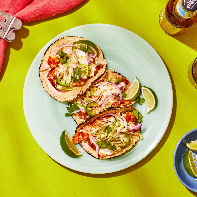 Plate of three fish tacos on a lime green table. 