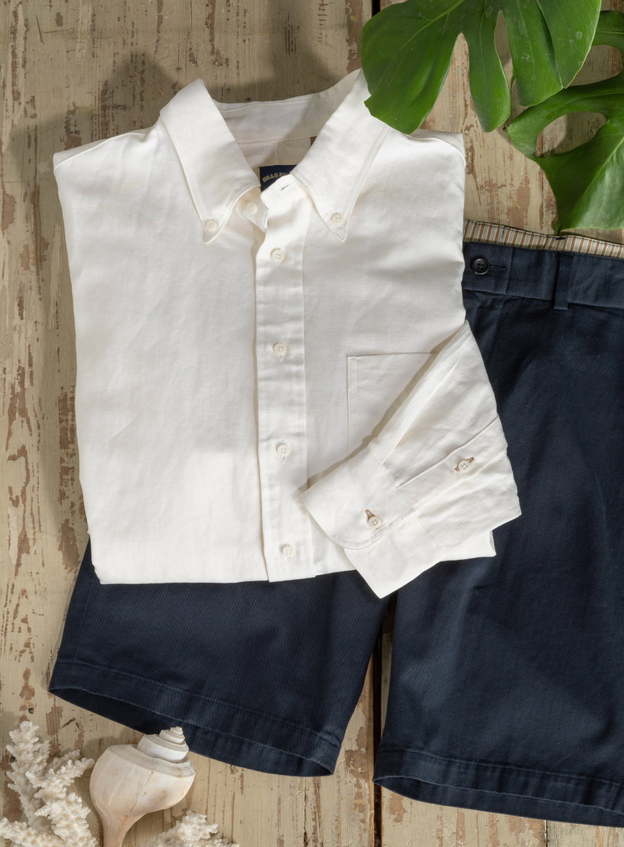 A natural cotton shirt and Bills Khakis shorts lay on a wooden surface surrounded by some beach objects
