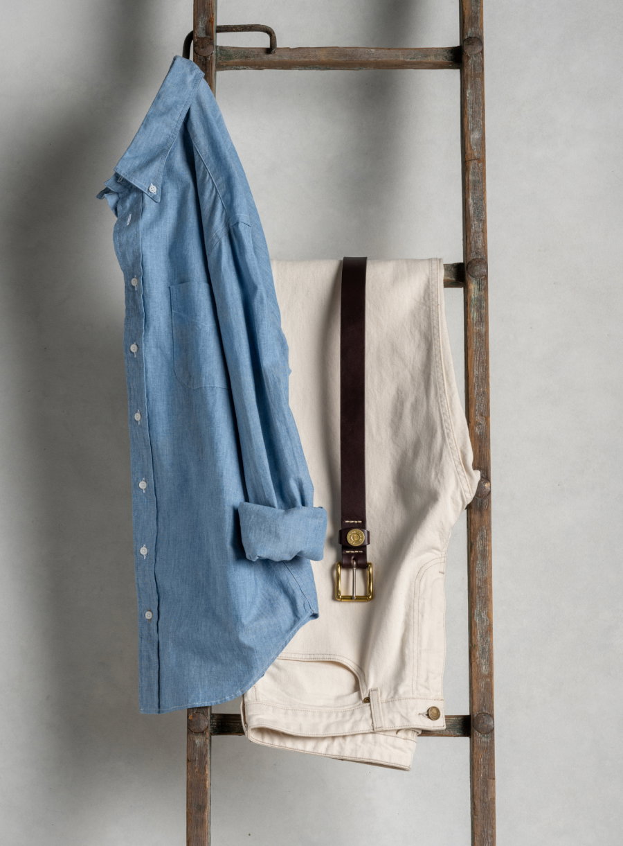 A Bills Khakis Chambray Denim shirt and pair of Bills Khakis pants + Belt hang from a vintage ladder