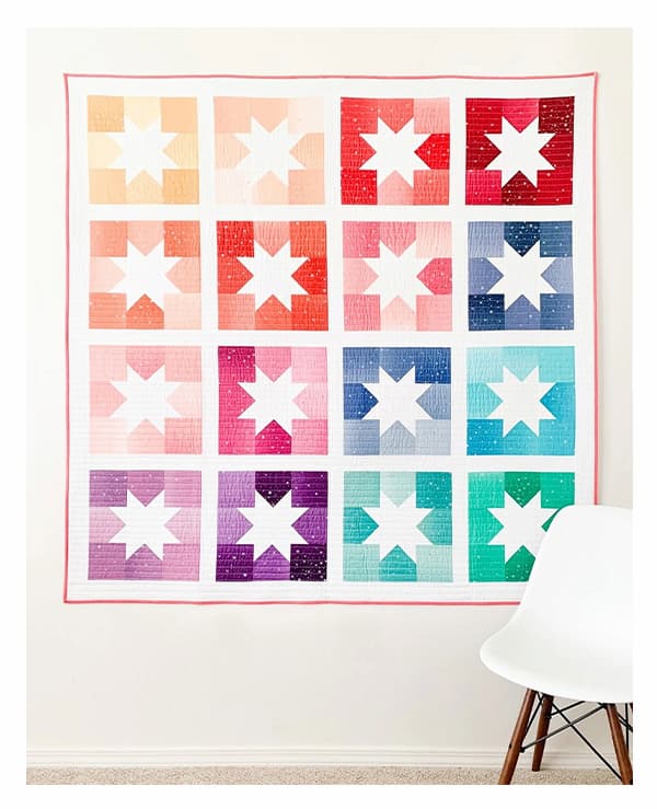 A quilt hanging on a wall, featuring bright blocks with white stars. >>