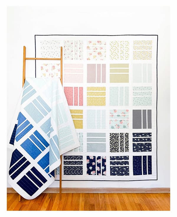 A quilt hanging from a wall, featuring squared up blocks of rectangular pieces, and a second quilt draped over a blanket ladder. >>