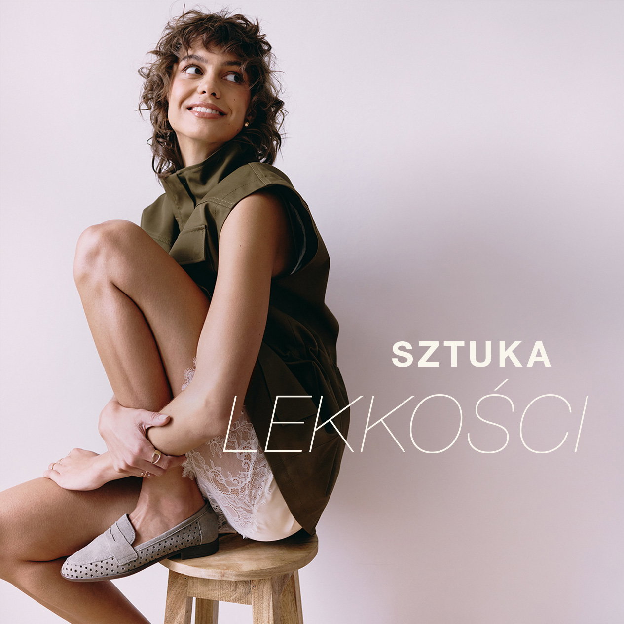 Smiling woman in stylish outfit sitting on stool with 'Sztuka Lekkości' text