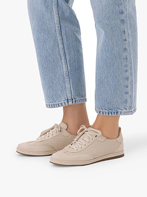 Woman wearing beige trainers with light blue jeans on a white background.