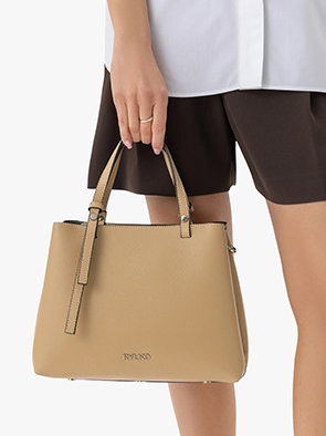 Woman holding a beige leather handbag with a white shirt and black shorts.