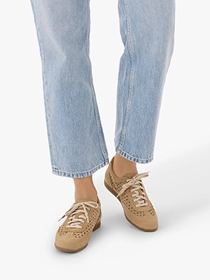 Person wearing light blue jeans and beige perforated trainers on a white background.