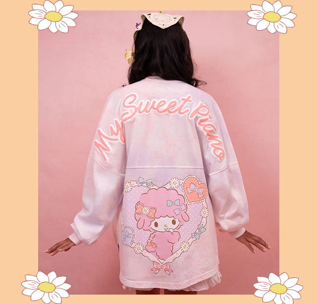 My Sweet Piano Spirit Jersey on model against a pink background with floral graphics. | This soft tie-dyed My Sweet Piano Spirit Jersey is the perfect wear-everywhere long sleeve for My Sweet Piano fans. It features her adorable face on the front, complete with colorful bows in her hair for an extra sweet touch. 