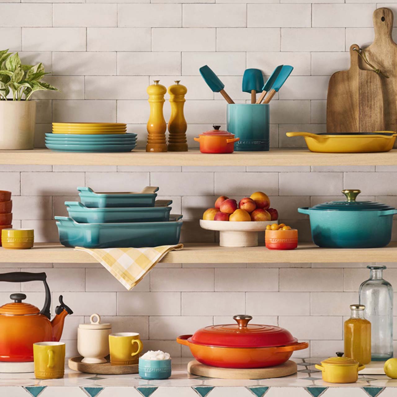 Colorful kitchenware on shelves, including pots, pans, plates, and utensils in shades of teal, orange, and yellow, with cutting boards and plants.