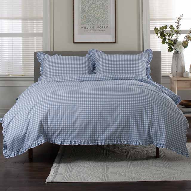 A bed with blue gingham-patterned bedding, flanked by nightstands with plants, under a framed artwork.