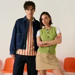 Jonge man en vrouw staan voor oranje stoelen, dragen casual lenteoutfits met sneakers, neutrale achtergrond.