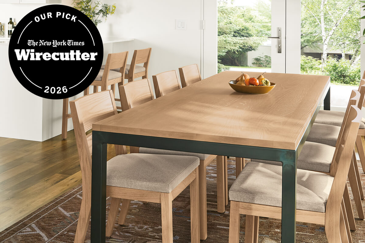 Parsons table with oak surface, green metal frame and upholstered dining chairs in a bright dining room.