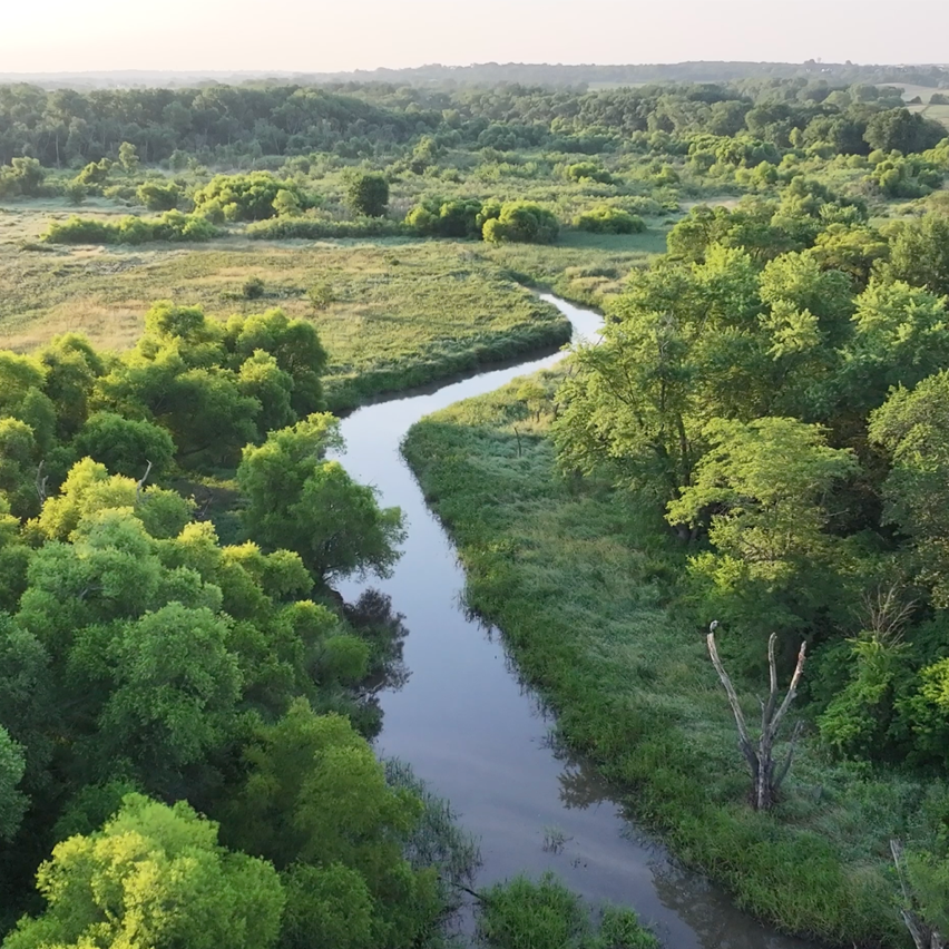 Aerial view of a winding river through lush green forests and hills.