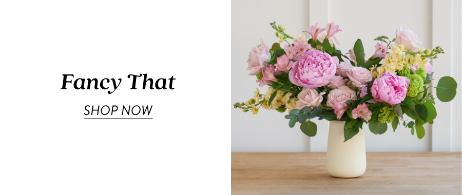 Product feature for “Fancy That,” showing a pink, peach, green, and white floral arrangement in a white vase on a tabletop, with a “Shop Now” link.