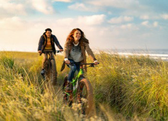 Una mujer y un hombre recorren la costa en bicicleta. Reserva ahora unas vacaciones activas. Descubrir todos los destinos.