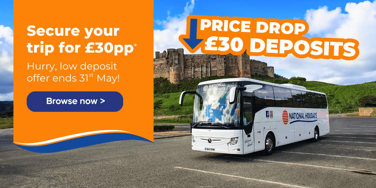 A coach with a "National Holidays" logo parked near a historic castle under a blue sky.
