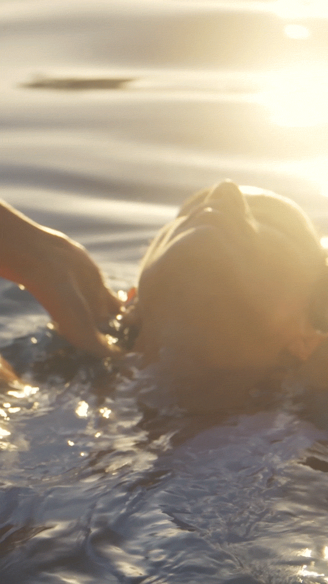 Animated GIF. A swimmer glides through open water at golden hour wearing Dorsey enamel necklace.