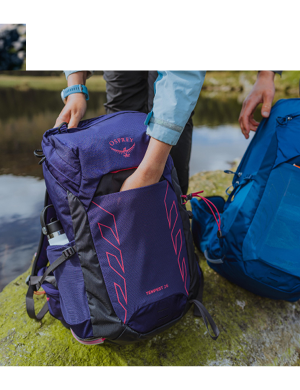 A woman reaches her hand into an Osprey Tempest 22L Rucksack in Purple.