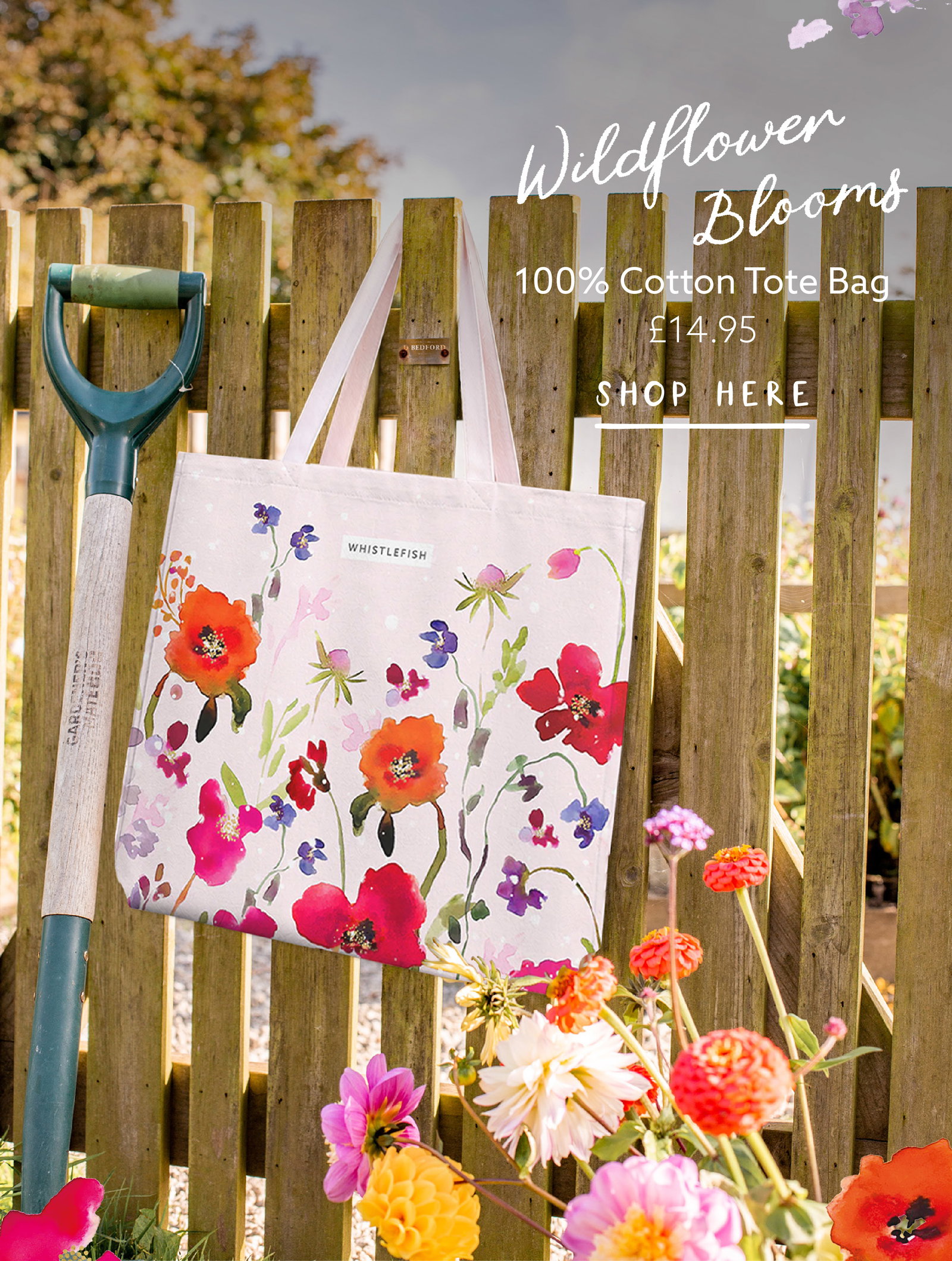 Wildflower Whispers cotton tote bag hanging on a garden fence surrounded by colourful summer flowers.